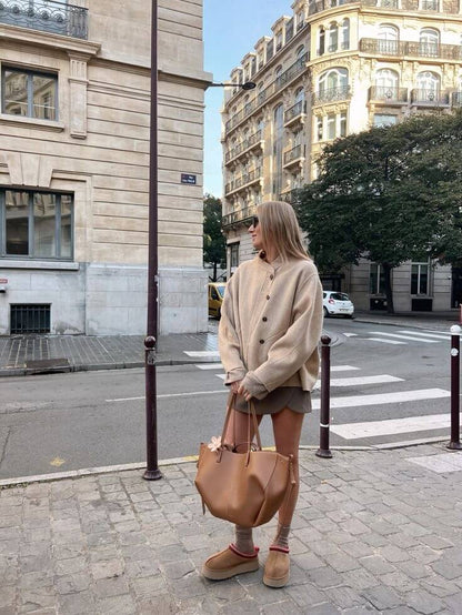 Eine frau in einem beigen pullover steht auf einer straßen in der stadt mit einer braun ledertasche