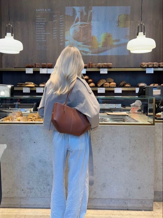 Eine frau mit langen haaren steht an einem café-theke mit einer braun ledertasche